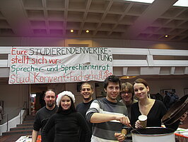 Fotos auf denen man einen Stand im Foyer der Hublandmensa sieht, Mitglieder der Studierendenvertretung geben Flyer und Glühwein aus