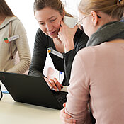 Anregende Unterhaltung zwischen zwei Teilnehmerinnen, während beide gemeinsam auf den Laptop-Display schauen. 