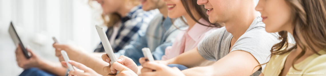 College friends sitting on the floor and watching pics on their gadgets at break. Side view.