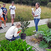 Schülerinnen und Schüler auf der Nutzpflanzenterasse gemeinsam mit einer Studentin. Eine Schülerin kniet an einem Orangenbäumchen und riecht an den Früchten.