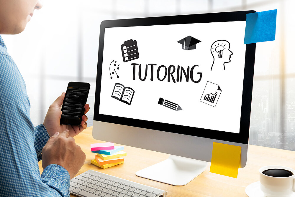 Person sitzt vor einem Bildschirm, auf dem das Wort "Tutoring" und verschiedene Lernsymbole sichtbar sind.