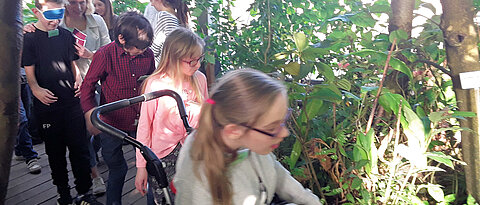 Kinder bewegen sich durch das Gewächshaus, im Vordergrund Mädchen im Rollstuhl.