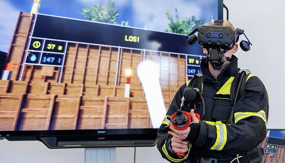 Alexander Schweigert, Lehrkraft an der staatlichen Feuerwehrschule Würzburg, demonstriert mit VR-Brille und einem Hohlstrahlrohr mit VR-Technik das virtuelle Training zur Innenbrandbekämpfung. 