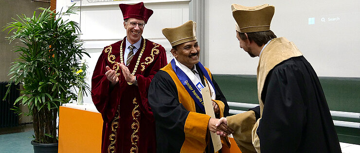 Dekan Holger Helten (re.) und Präsident Paul Pauli (li.) gratulieren Professor Jarugu Narasimha Moorthy zum Erhalt der Ehrendoktorwürde.
