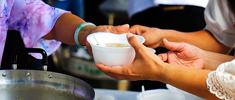 Woman handing another woman a soup bowl.