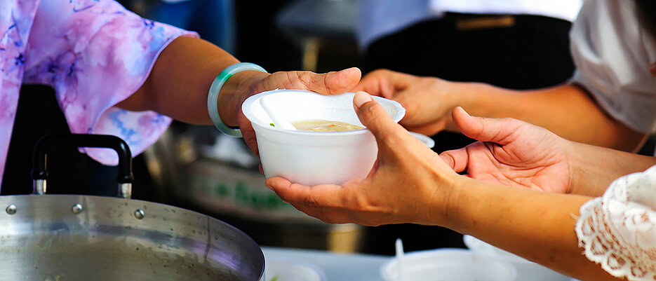 Woman handing another woman a soup bowl.